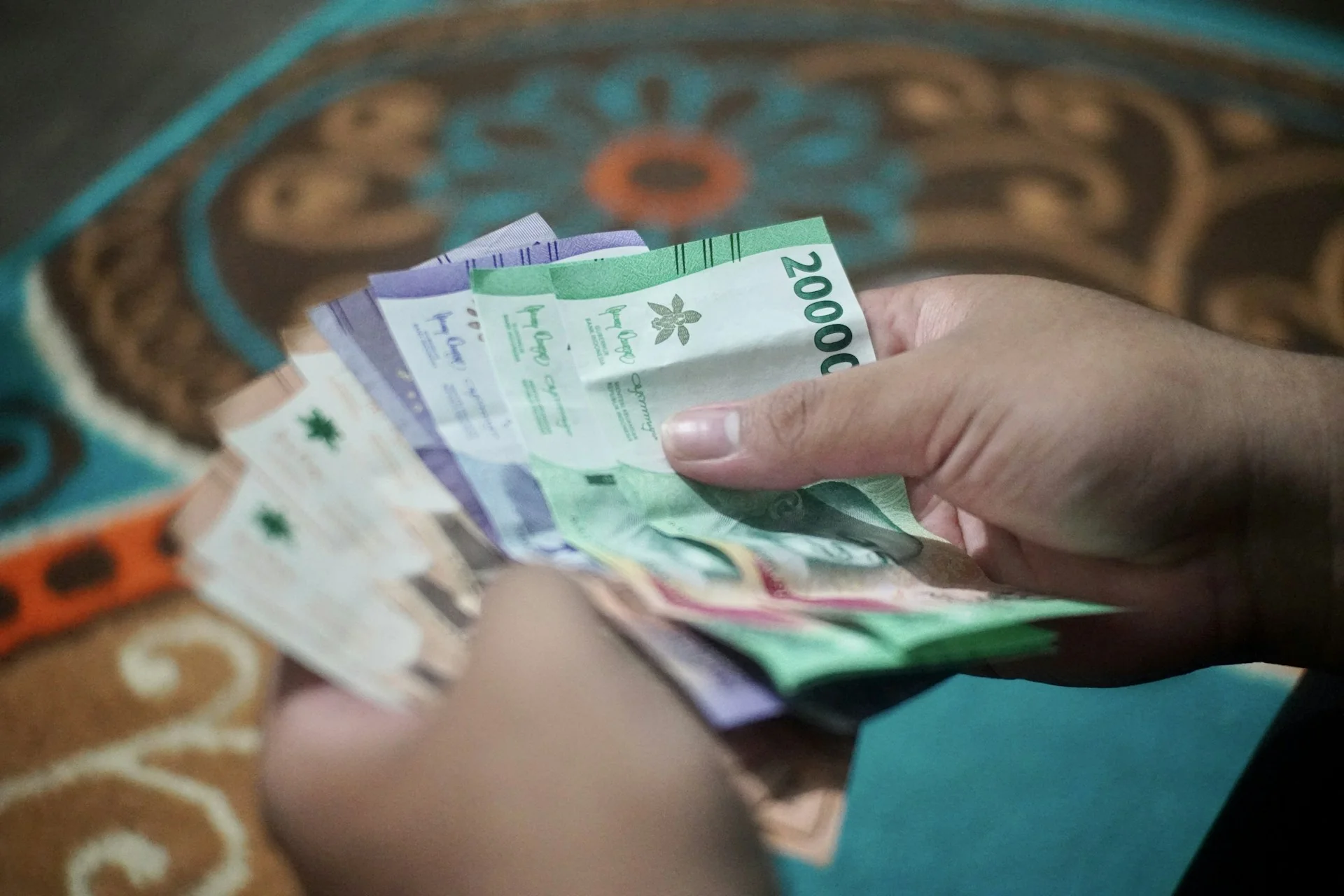 Dua tangan menghitung lembaran uang rupiah pecahan Rp20.000 dan lainnya di atas karpet bermotif
