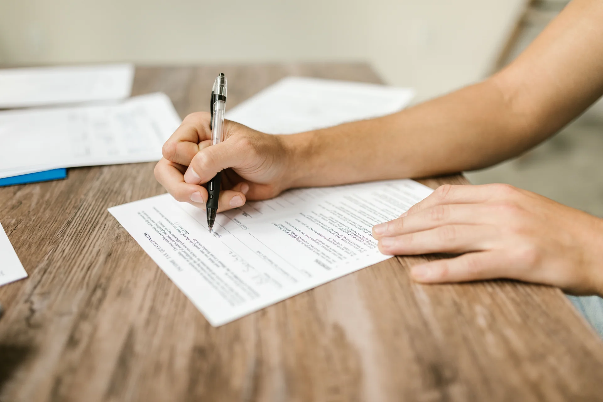Tangan mengisi formulir kertas dengan pena di atas meja kayu