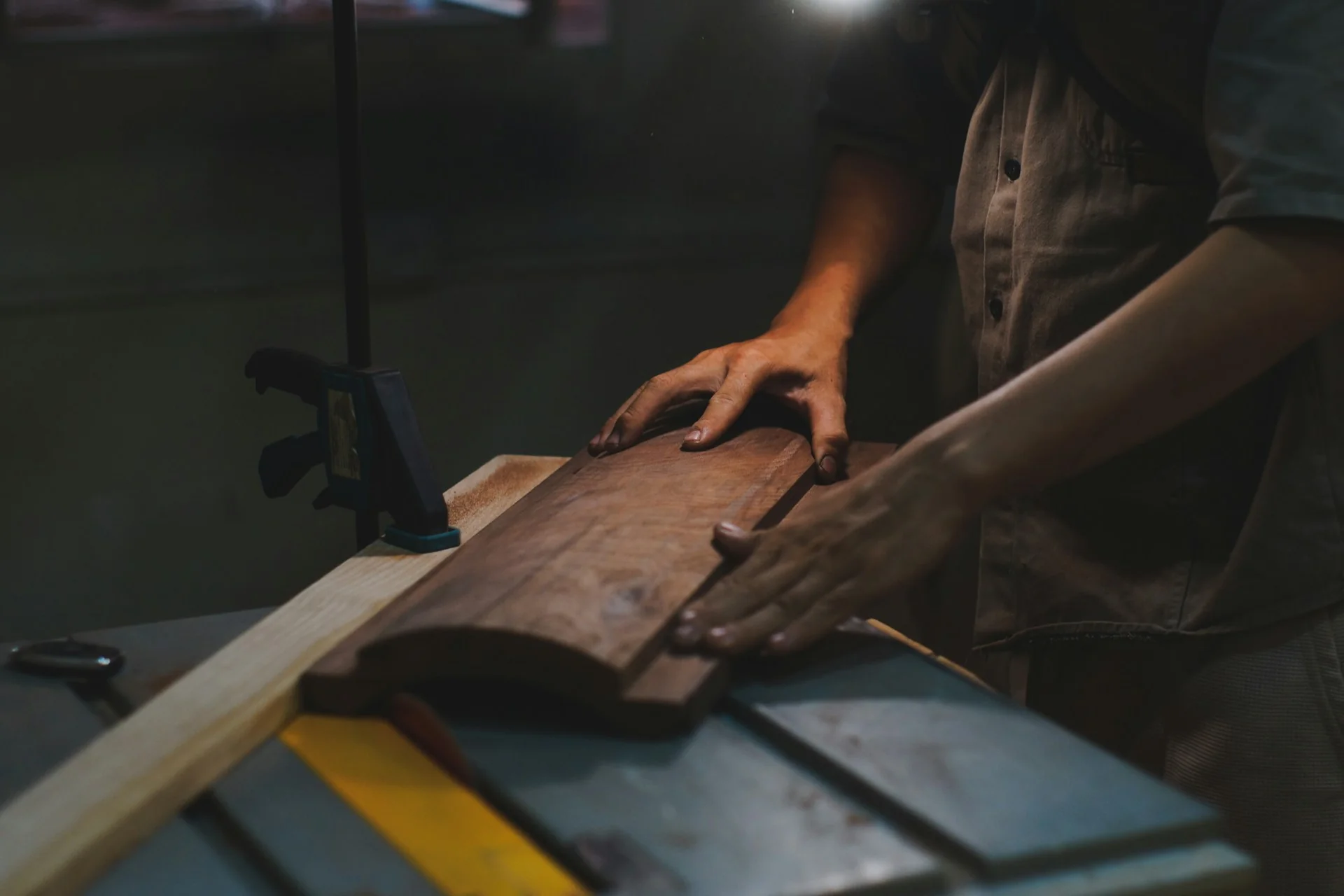 Tangan tukang kayu mendorong papan kayu di atas gergaji meja di bengkel