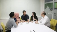Lima karyawan berdiskusi di meja putih ruang rapat kantor kecil