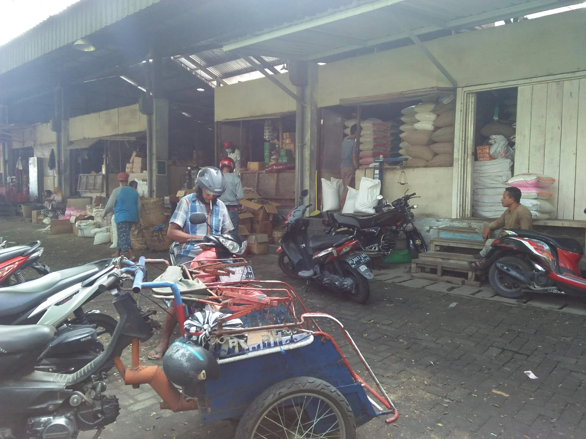 Deretan toko sembako dengan tumpukan karung beras dan sepeda motor pembeli di Pasar Induk Pare, Kediri