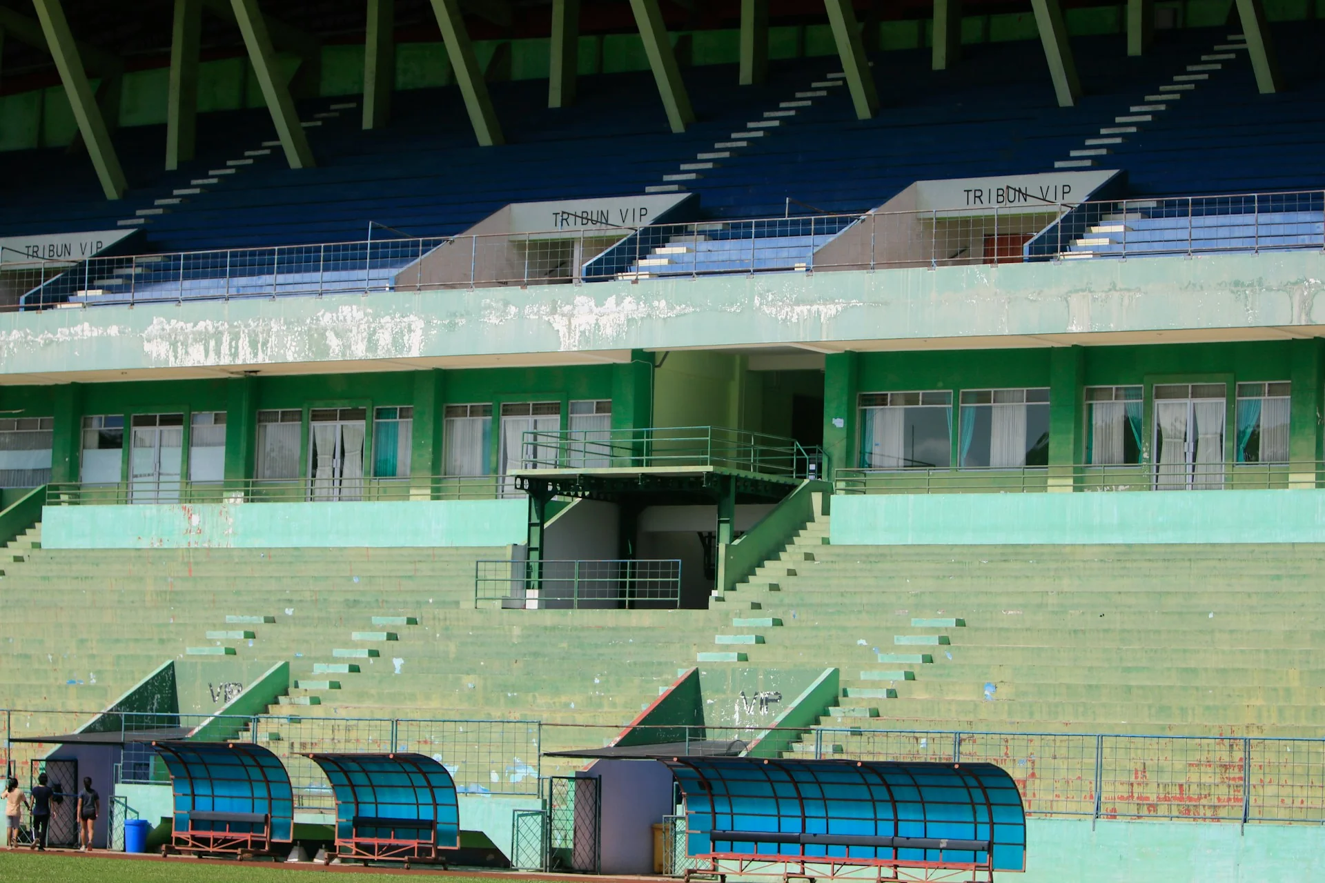 Tribun stadion sepak bola yang kosong dengan bangku cadangan beratap biru di tepi lapangan