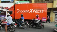 truk-shopee-xpress-pengiriman-paket Truk oranye Shopee Xpress terparkir di tepi jalan dengan beberapa pengendara sepeda motor di depannya