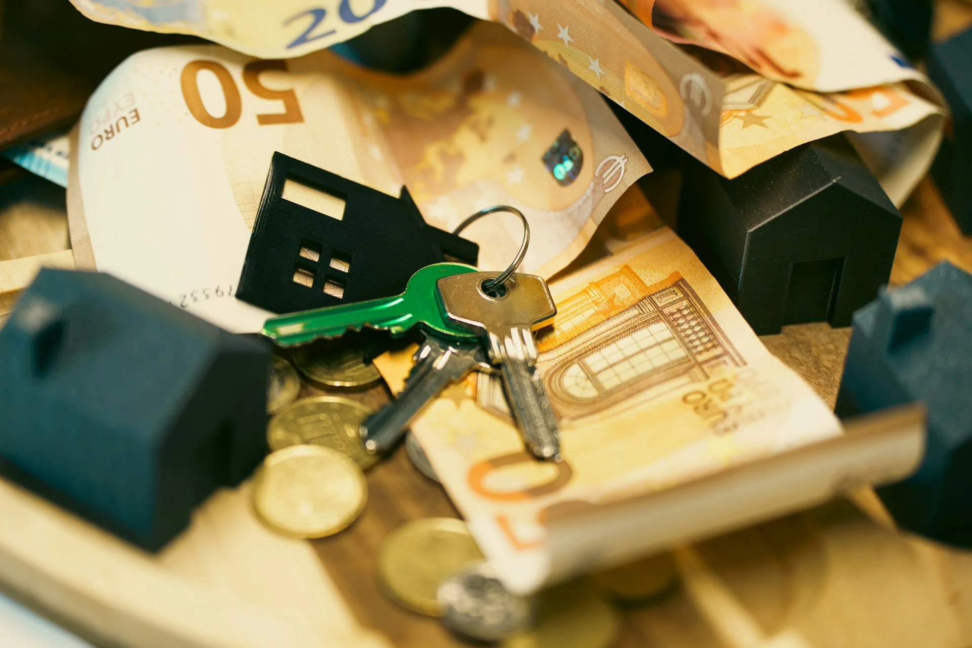 Uang kertas dan koin euro, kunci rumah, serta miniatur rumah sebagai ilustrasi aset bergerak dan tidak bergerak