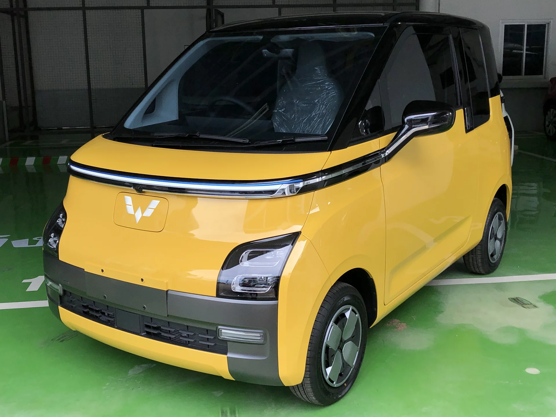 Mobil listrik Wuling Air ev Long Range warna kuning dengan atap hitam di area parkir